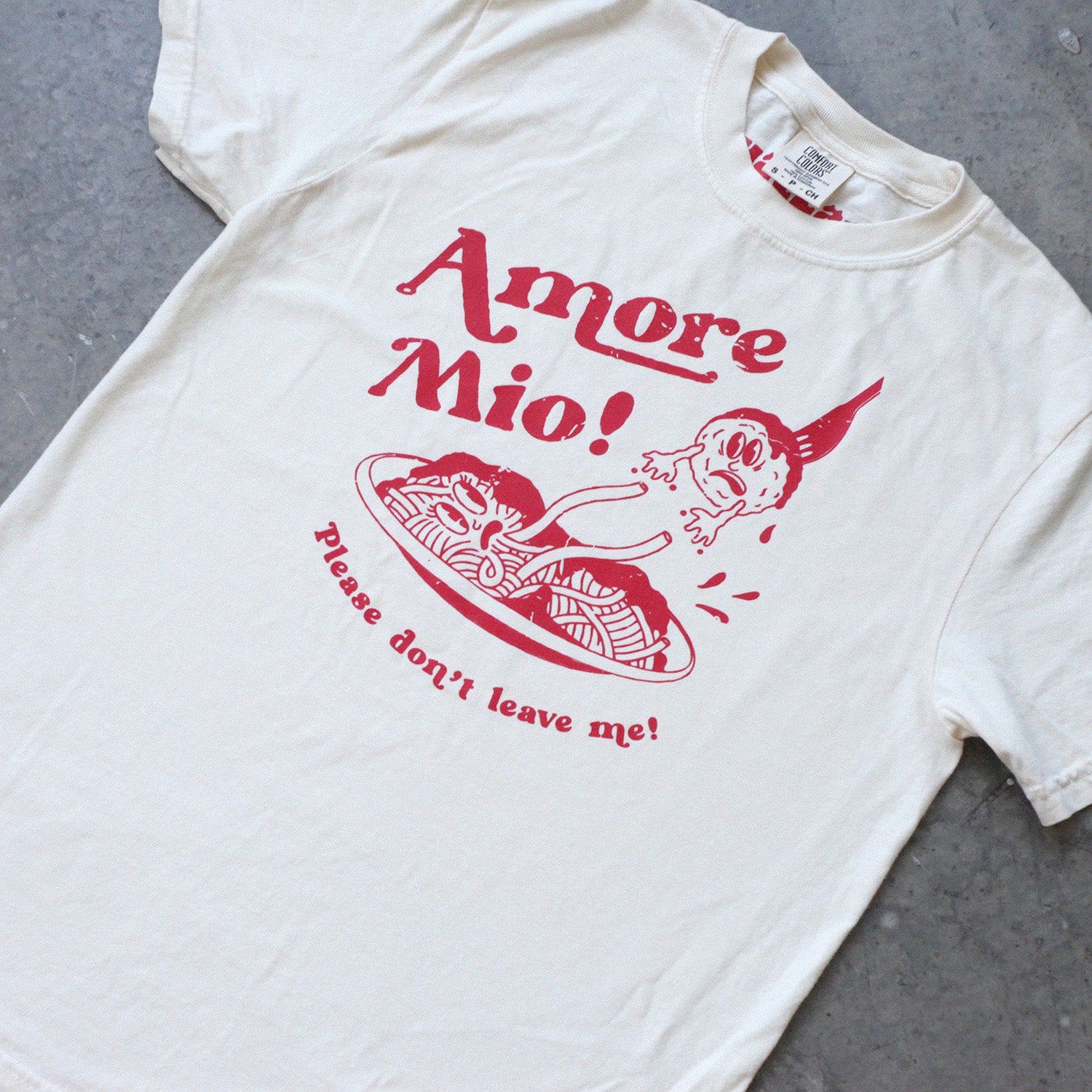 Graphic tee shirt with a red spaghetti and meatball design that reads "Amore mio, please don't leave me" on it