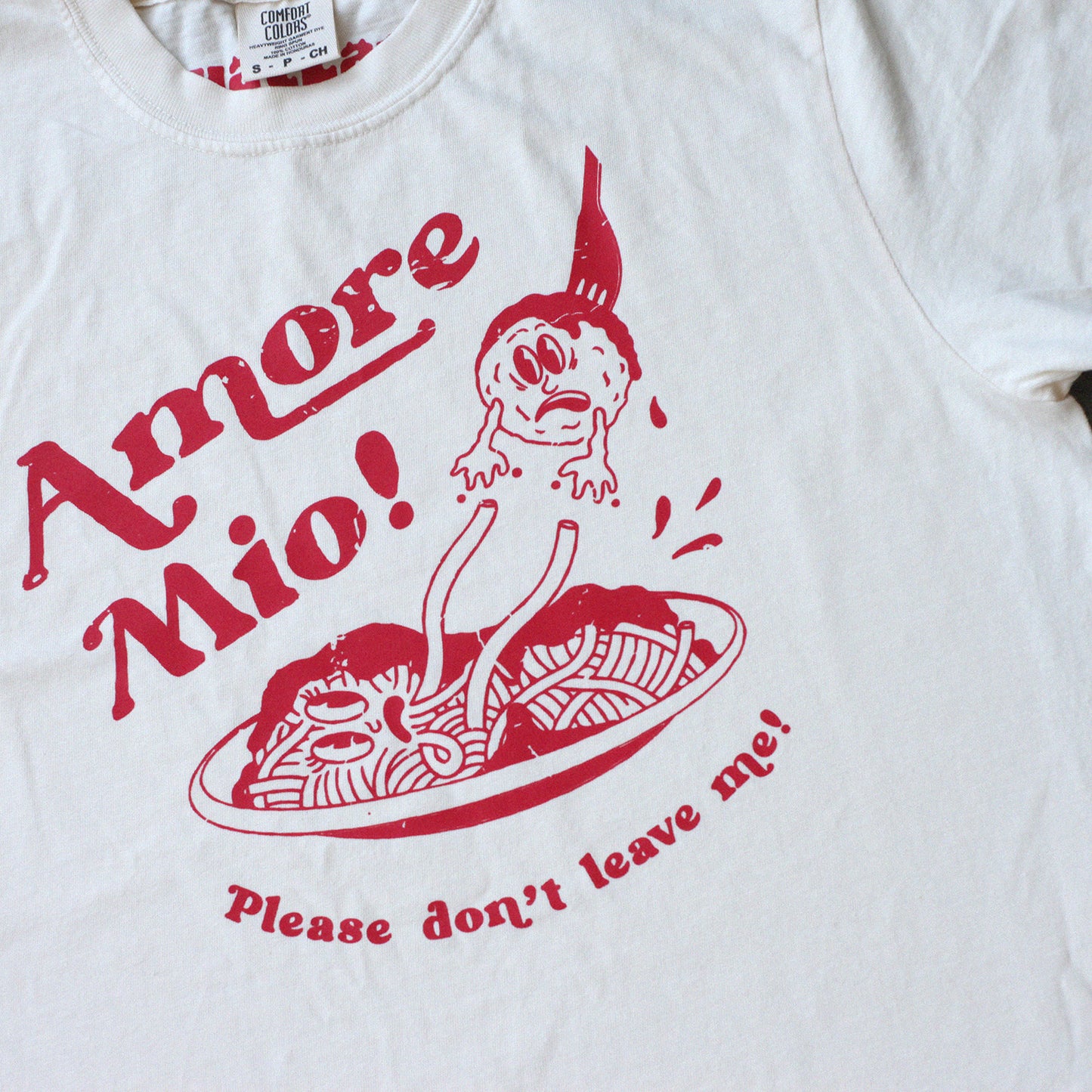 Graphic tee shirt with a red spaghetti and meatball design that reads "Amore mio, please don't leave me" on it