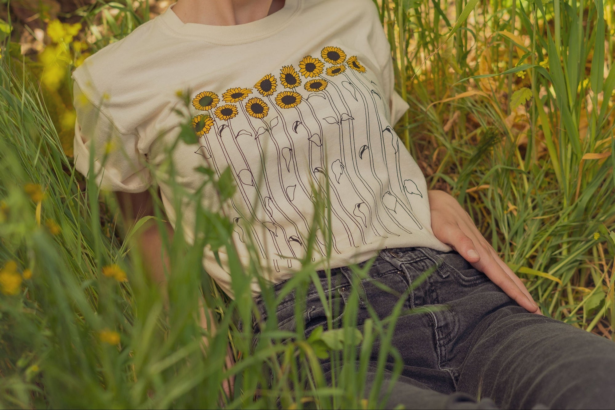 A person sitting in a field wearing a sunflower tee shirt